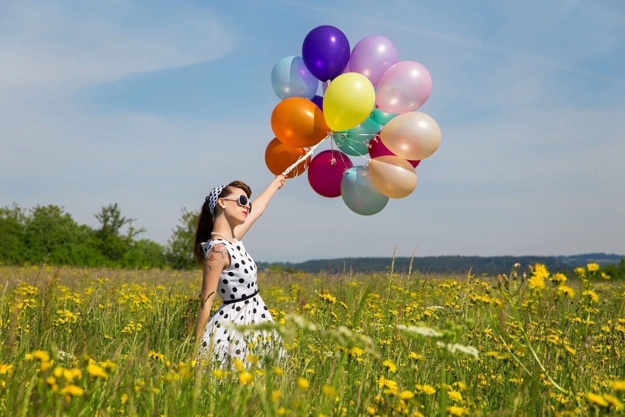 young woman with a white rockabilly dot dress and a lot of colorful balloons in the meadow
